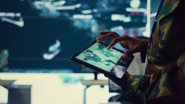 Armeijan sotilas tarkastelee kohteita laitteelta, jossa maailmankartta.